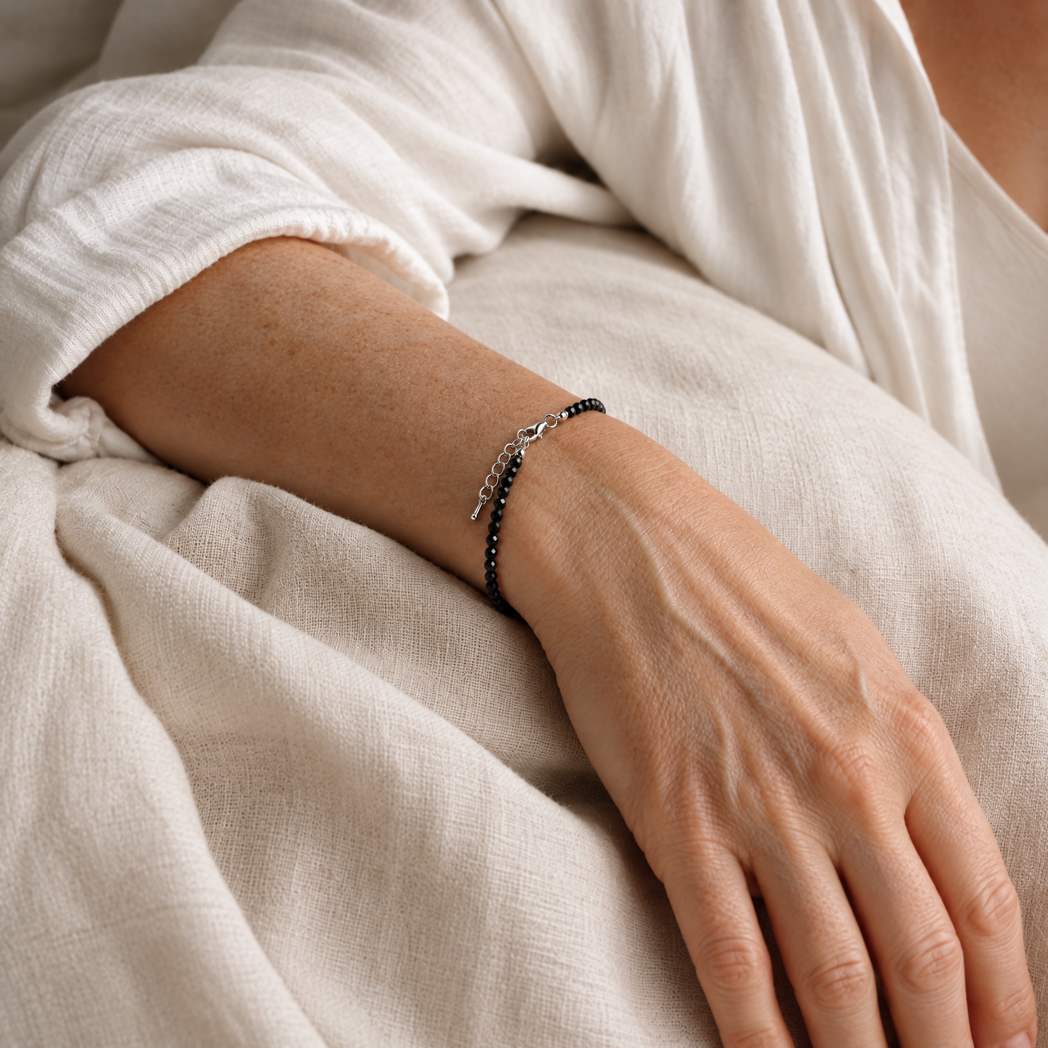 Woman wearing the thin black obsidian bracelet, arm resting on white linen