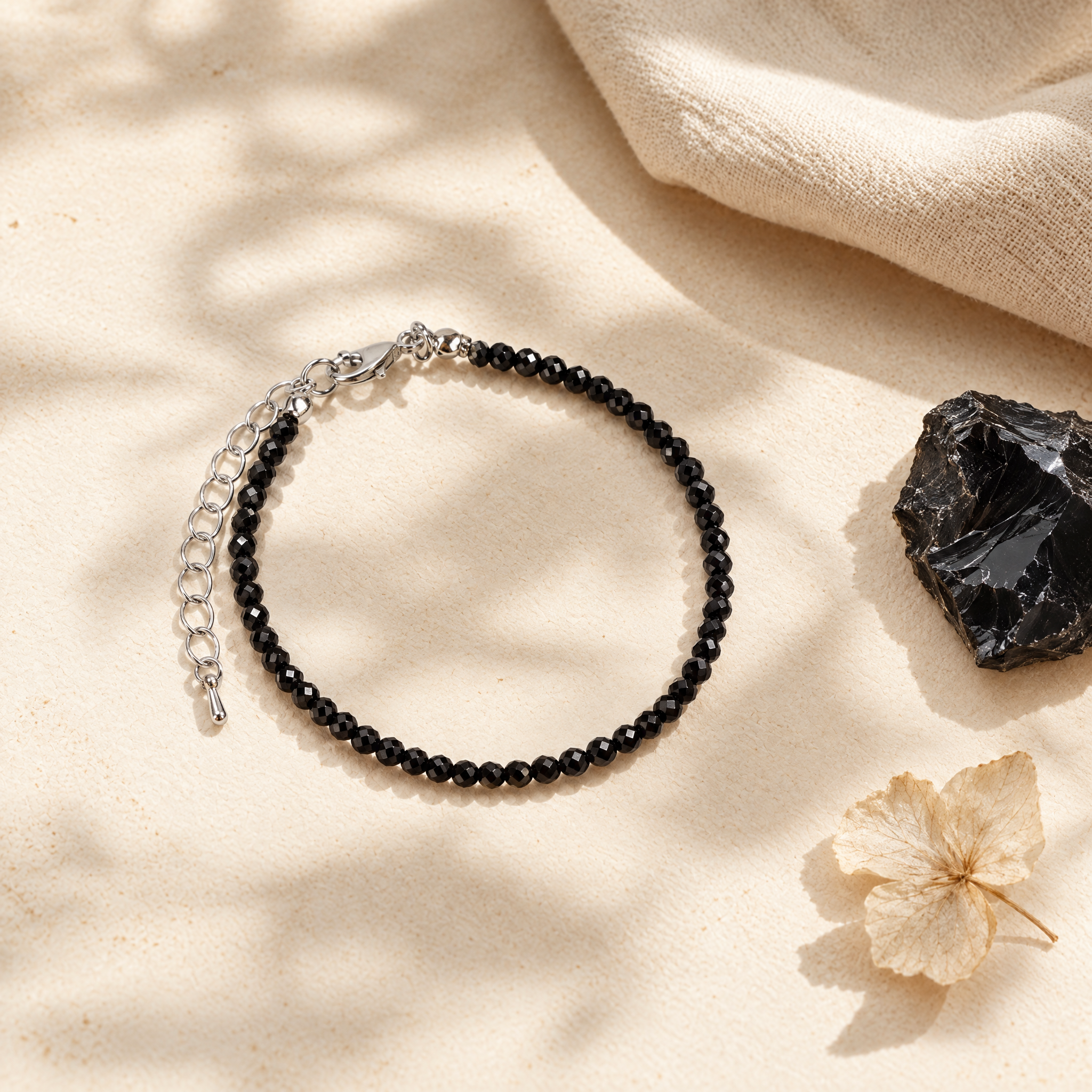 Black obsidian bracelet in a soft flat-lay with linen and a raw stone